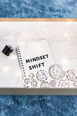 law of attraction, box as metaphor of the mind with idea light bulb and gear mechanism with Mindset Shift notepad and fairy lights