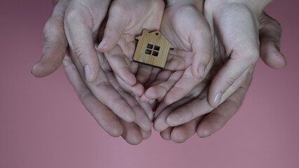 The hands of the mother and father with the child hold the figure in the form of a house on a pink background.