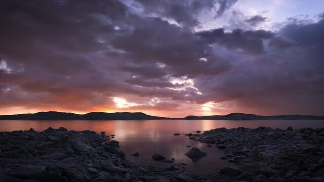 Dramatic lake scene at sunset with a stormy sky and a warm golden glow on the horizon. A calm, tranquil and serene, natural landscape.  