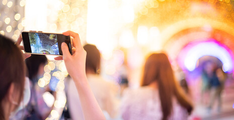 Girl hand holding mobile phone taking the light tunnel decorated for the Christmas and New Year Celebration,