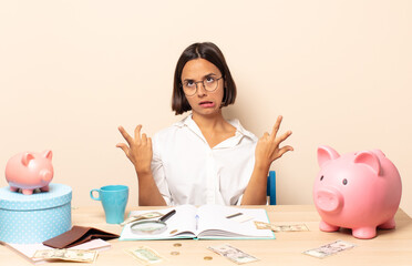 young latin woman shrugging with a dumb, crazy, confused, puzzled expression, feeling annoyed and...