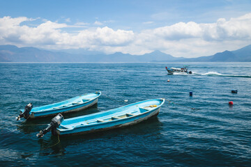 Two blue boats and speed boat passing by on lake Atitlan with view on volcanoes in Santa Cruz la Laguna, Guatemala