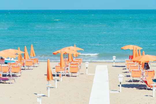 Sunbeds and parasols on the seashore. Beach, sea and umbrellas on summer day. Adriatic coast, Rimini, Italy, view from Gabicce Mare.