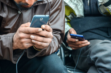 Refugees from Syria using mobile phones in camp to contact their families. People using smart phones. Man texting and surfing on the phone. Holding smartphone.