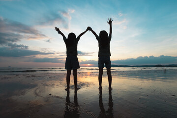 Silhouette of two asian child girls playing on the beach together at the sunset time with beautiful sea and sky. Family enjoy with nature concept.