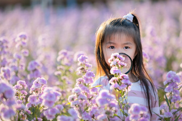 Cute asian little child girl holding magnifier looking on flower with curiously and enjoying with beautiful flower in the flower garden.
