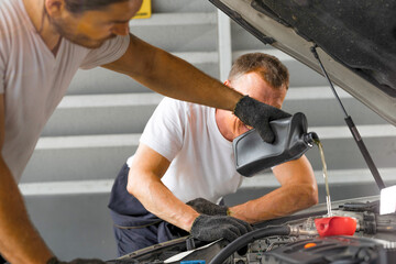 worker men repairing is pouring Motor oil in engine vehicle at petrol pump garage repairing center....