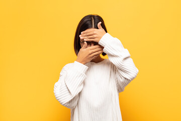 young latin woman covering face with both hands saying no to the camera! refusing pictures or...