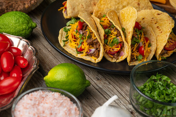 Close-up view of plate with hot mexican tacos on rustic wooden table with ingredients for cooking background. Concept of traditional meal. Appetizing photo for menu or cookbook.