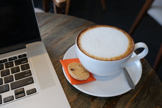 A cup of cappuccino coffee or latte coffee in a white cup with laptop on table. Royalty high quality free stock photo of drink capuccino or latte coffe with laptop for working in office