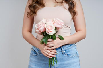 Portrait of a beautiful headless woman in a pink T-shirt, jeans with a bouquet of pink roses. Studio shot on gray background. Holiday concept of valentine's day, birthday, mother's day, womens day. - obrazy, fototapety, plakaty