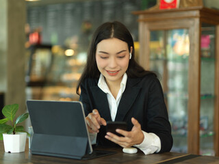 Businesswoman take a break with smartphone while working with tablet in cafe