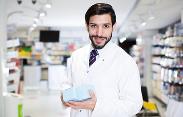 Fototapeta premium Happy male specialist who is holding medicines near shelves in pharmacy