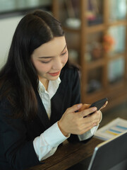 Female office worker relaxing with smartphone while working in cafe