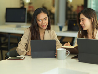 Two female office workers brainstorming on their work with digital tablets in meeting room