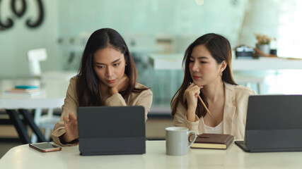 Two female office workers working with digital tablets in meeting room