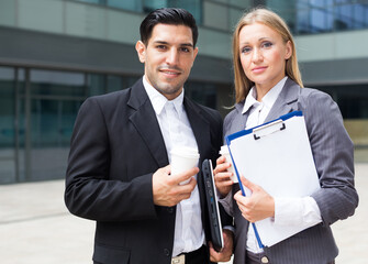 Businessman and his woman colleague in suit are standing with folder and coffee near the office.