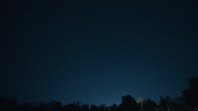 Shooting star passes through the sky over an empty basketball court at night.