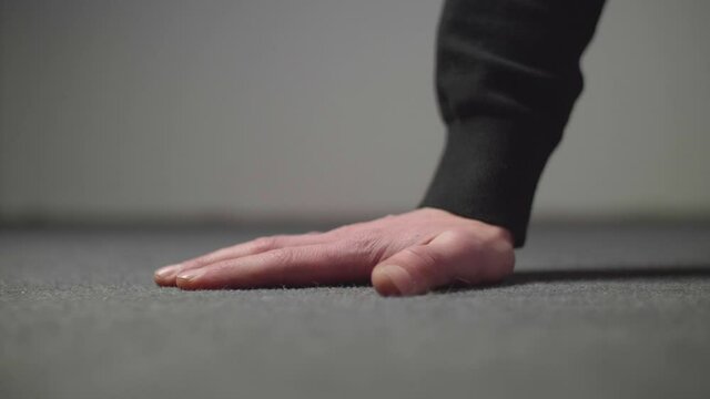 Male caucasian hand touching a gray floor surface with a neutral gray background. Close up in 4K.