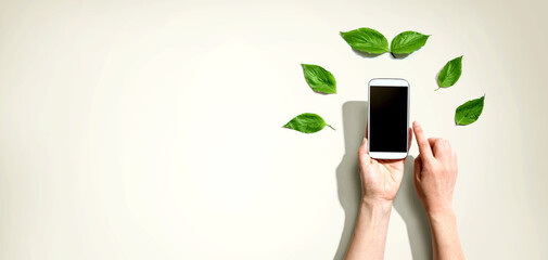 Person holding a smartphone with green leaves