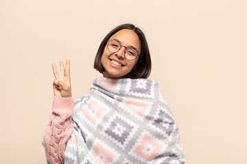 young latin woman smiling and looking friendly, showing number three or third with hand forward,...