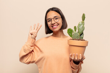 young latin woman smiling and looking friendly, showing number four or fourth with hand forward,...