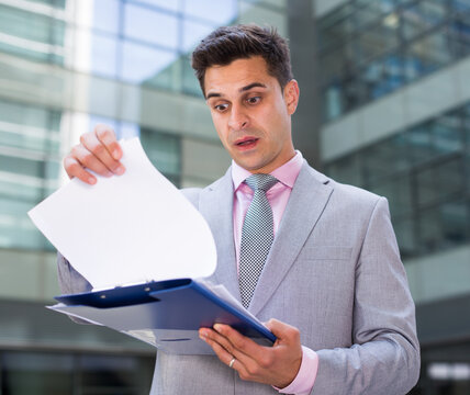 Surprised and shocked businessman reading documents on plant background
