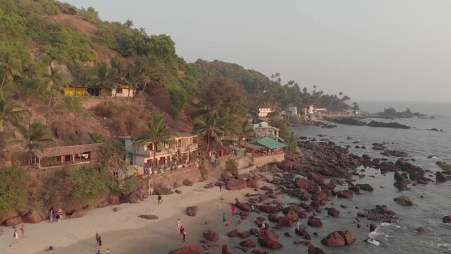 Exotic Guesthouse near rocky shoreline in Arambol Beach in North Goa, India - Aerial dronie fly away wide shot