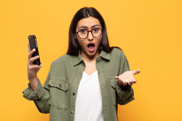 young latin woman open-mouthed and amazed, shocked and astonished with an unbelievable surprise