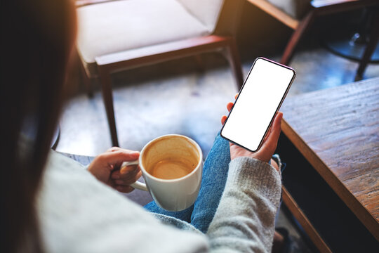 Mockup image of a woman holding mobile phone with blank white desktop screen while drinking coffee