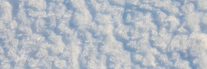 Beautiful winter background with snowy ground. Natural snow texture. Wind sculpted patterns on snow surface. Wide panoramic texture for background and design.