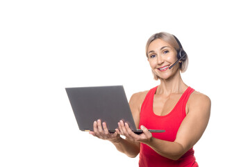 Fototapeta premium Distance fitness coaching. Smiling Caucasian attractive woman in sportswear with headset and microphone is live streaming online, laptop in hands, isolated on white.