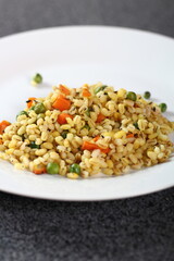 Cooked pearl barley with carrot and green peas on plate