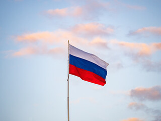 Russian tricolor flag waving in the wind against a blue sky.