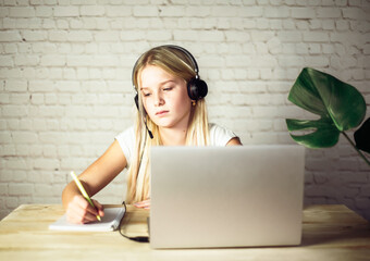 Children home schooling, teenage girl in headphones studying online at home, e-learning concept