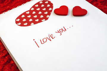 on a red openwork background is a notebook on which it is written i love you. valentine's day.