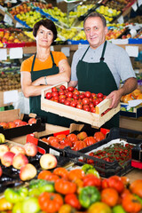 Mature man and woman sellers are demonstraiting red tomatos in the store
