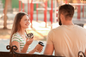 Young couple eating sweet donuts and drinking coffee outdoors
