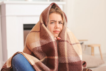 Young woman wrapped in warm plaid at home. Concept of heating season