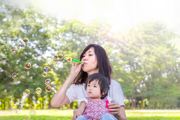 緑の樹木を背景に公園でシャボン玉で遊ぶ親子