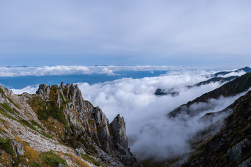 View of rocky mountain range and valley engulfed in clouds on the horizon in early autumn at Senjojiki Cirque in Nagano Prefecture, Japan.