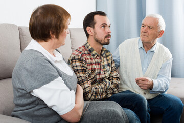 Elderly grandfather talking seriously with his grandson in presence of grandmother