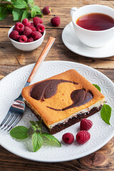 A piece of double-layer cake on a plate of chocolate brownies and curd cheesecake with raspberries. copy space