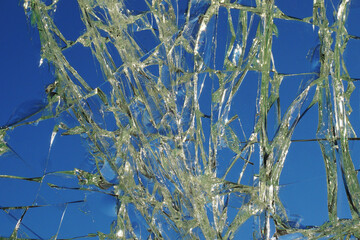 Broken glass with cracks and sun glare on the background of the blue sky, background, texture.