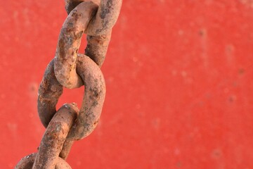 Weathered chain, rusty, with red painted background.  Off center.
