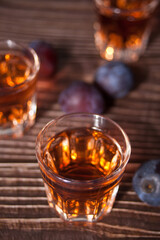 Plum vodka or brandy with fresh plums on the wooden table.
