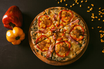 top view Traditional Italian pizza with bacon, paprika, caramelized onions and corn on a black rustic wood background. Top view of hot pizza.