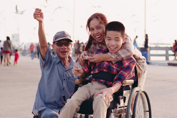 Asian Disabled child on wheelchair and parents the outdoors ​nature​ and seagull birds background​,Life in the education age of special children,Happy disability kid travel in family holiday concept.