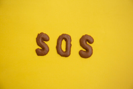 Word SOS arranged from homemade chocolate cookie  alphabet on yellow table