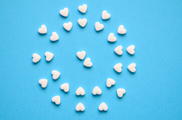 white heart-shaped tablets close up in form of circle on  blue background with copy space. Concept of Valentine's day, medical Flatlay. Card to day of doctor. world pharmaceutical day